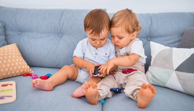 Beautiful toddlers sitting on the sofa playing with toys at home
