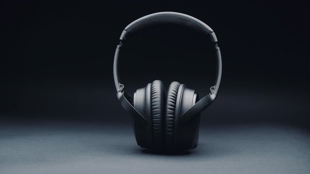 A Product Shot Of Black Headphones On A Black Background, Standing Upright. Camera Movement From Right To Left.