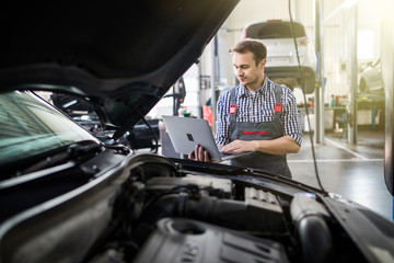 Smiling young man mechanic using a laptop computer to check a car engine