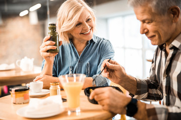 Happy pretty adult woman showing smoothie bottle for man