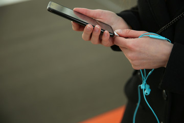 woman's hands holding smartphone and earphones close-up with copy space