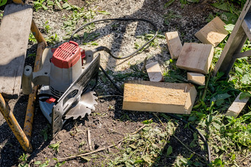 an electric manual circular saw is lying on the ground near scraps of wood planks with non-compliance with safety regulations