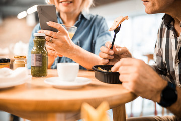 Woman holding mobile phone during lunch with man