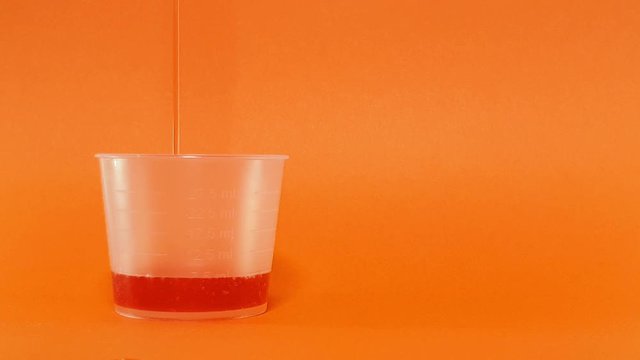 Red liquid medication poured from out of shot into a dose cup against a Corel background