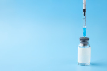 Medical glass bottle with copy space, with syringe inserted, on a blue background. Selective focus....