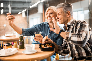 Happy mature man and woman looking at phone camera in cafe