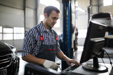 Portrait of happy male mechanic touching computer monitor in auto repair shop