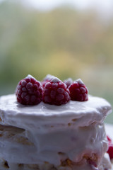 Frozen raspberries on a cake, drizzled with white cream, on a blurred natural background.