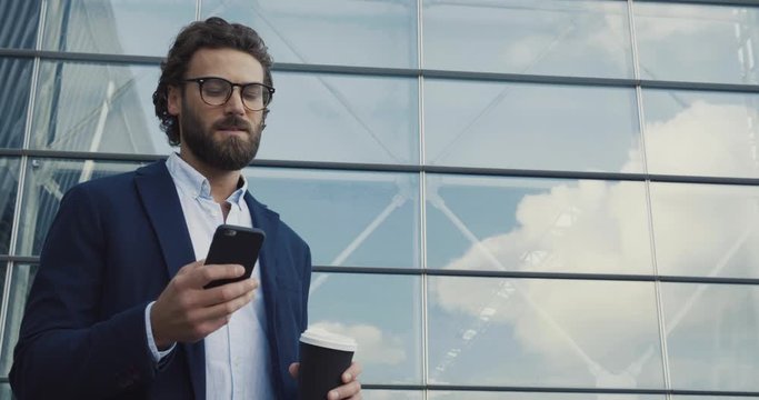 Handsome bearded Startup Businessman in Glasses using mobile Phone. Young man texting Messages, cheating on his Smartphone while walking in Office District. Business. Social Networking. People. Apps.