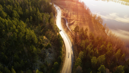 Aerial view of winding road through forest with blue lakes in Finland at sunset.
