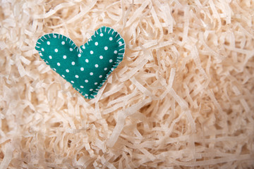 A heart sewn from green fabric lies on artificial straw. DIY made.