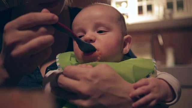 Mom feeds hungry baby in bib with spoon, close-up