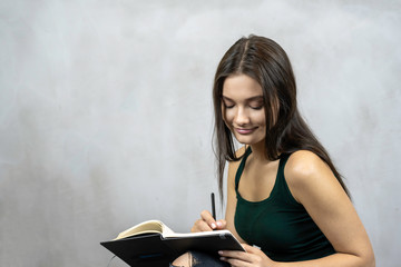 Young pretty woman with pen and note book writing on grey background. copy space
