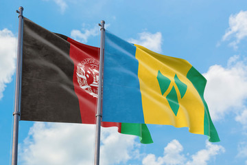 Saint Vincent And The Grenadines and Afghanistan flags waving in the wind against white cloudy blue sky together. Diplomacy concept, international relations.