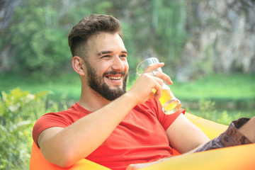 bearded smiling man in a t-shirt with a drink relaxes in nature