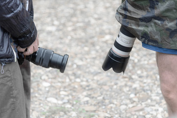 two digital cameras with zoom lenses in the hands of photographers