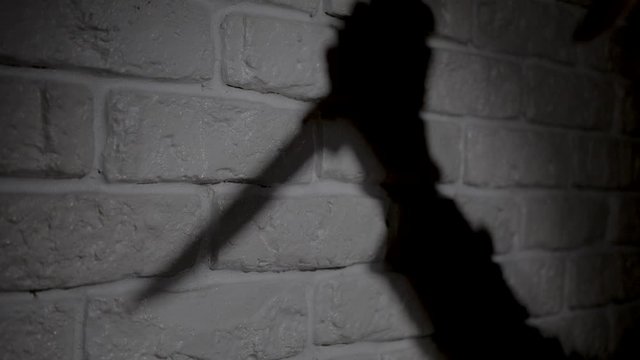 Knife is crawling in night. Shadow reflection of a hand with a knife on the wall.