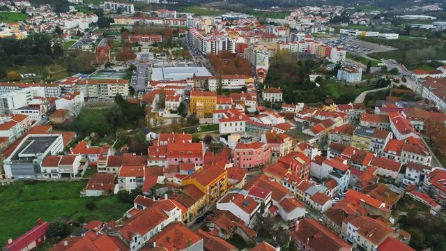 Drone footage of orange rooftop buildings and houses in the European city of Alcobaca, Portugal on a cloudy day. Camera zooming in.