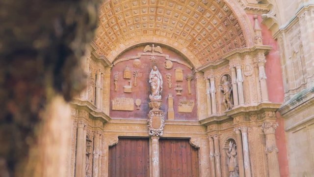 A close up view of beautiful antique old Catholic architecture art at the Palma Cathedral Roman Catholic Diocese of Majorca front entrance gate over the tree mud, Mallorca, Spain.