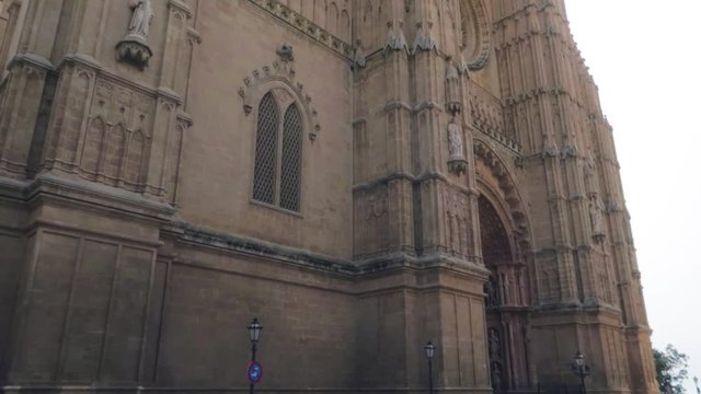 A low angle tilting down view of beautiful architecture of the Palma Cathedral Roman Catholic Diocese of Majorca front entrance gate over the tree, Mallorca, Spain.