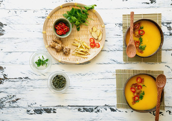 Freshly made creamy pumpkin soup served in coconut bowls with asian seasonings and pumpkin seeds