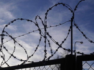 Silhouette of a fence with barbed wire against a blue sky. Prison security.