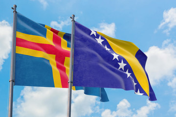 Bosnia Herzegovina and Aland Islands flags waving in the wind against white cloudy blue sky together. Diplomacy concept, international relations.