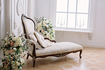 Rococo style sofa in a bright room near a vase of flowers and a large bright window with candlesticks