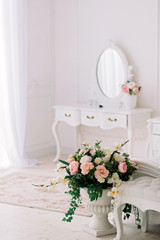 Rococo stone vase with flowers in a bright room on the background of a cosmetic table with a mirror. Interior Design.