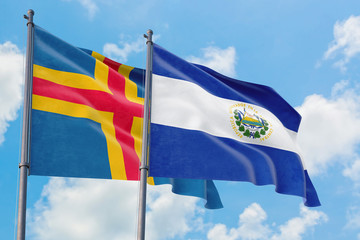 El Salvador and Aland Islands flags waving in the wind against white cloudy blue sky together. Diplomacy concept, international relations.