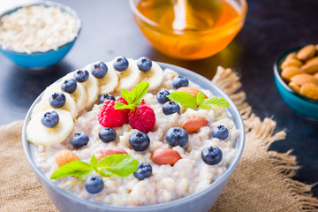 Oatmeal porridge with berries, fruits and honey on dark background. Oatmeal with raspberries, blueberries and almonds on burlap. Healthy breakfast
