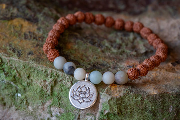 natural amazonite beads and rudraksha seed beads bracelet with lotus pendant on rocky background
