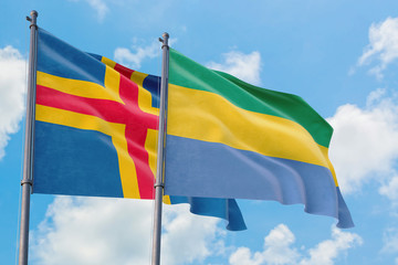 Gabon and Aland Islands flags waving in the wind against white cloudy blue sky together. Diplomacy concept, international relations.