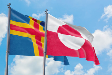 Greenland and Aland Islands flags waving in the wind against white cloudy blue sky together....