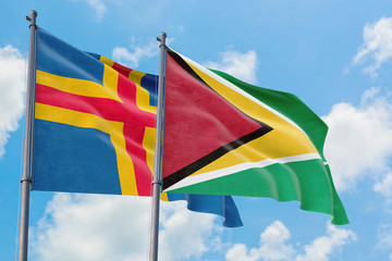 Guyana and Aland Islands flags waving in the wind against white cloudy blue sky together. Diplomacy concept, international relations.