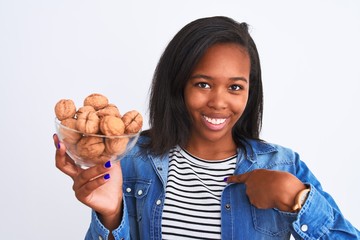 Young african american woman holding bunch of walnuts over isolated background with surprise face pointing finger to himself