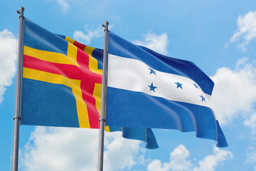Honduras and Aland Islands flags waving in the wind against white cloudy blue sky together. Diplomacy concept, international relations.