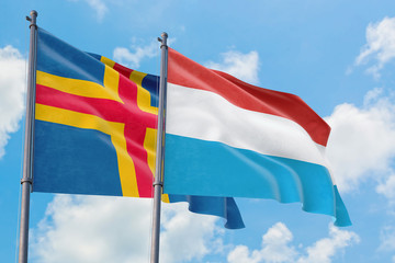 Luxembourg and Aland Islands flags waving in the wind against white cloudy blue sky together. Diplomacy concept, international relations.