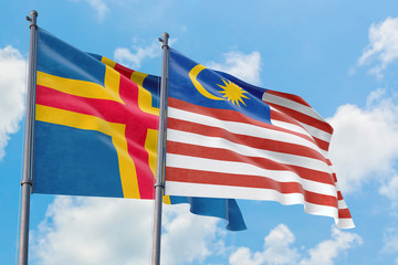 Malaysia and Aland Islands flags waving in the wind against white cloudy blue sky together. Diplomacy concept, international relations.