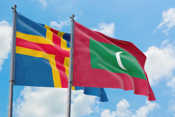 Maldives and Aland Islands flags waving in the wind against white cloudy blue sky together. Diplomacy concept, international relations.