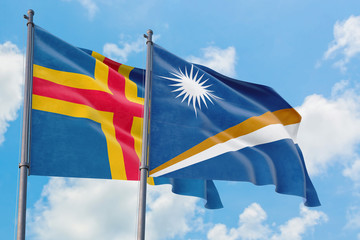 Marshall Islands and Aland Islands flags waving in the wind against white cloudy blue sky together. Diplomacy concept, international relations.