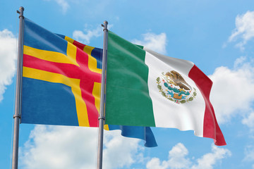 Mexico and Aland Islands flags waving in the wind against white cloudy blue sky together. Diplomacy concept, international relations.