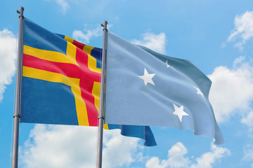 Micronesia and Aland Islands flags waving in the wind against white cloudy blue sky together. Diplomacy concept, international relations.
