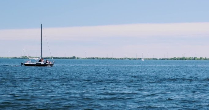 Slow motion shot of a small yacht floating through a bay with wind turbines spinning in the background
