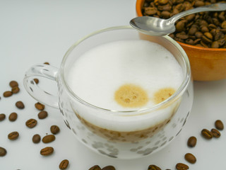 Double glass cappuccino near a bowl of coffee beans