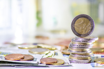 Stapel Euro-Münzen aus 2 Euro, 1 Euro und Cent-Münzen mit einem Haufen Bargeld aus Geldscheinen und EURO-Münzen zeugt von Reichtum in der Finanzwelt und schnelles Geld - obrazy, fototapety, plakaty