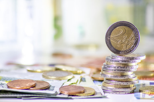 Stapel Euro-M&uuml;nzen aus 2 Euro, 1 Euro und Cent-M&uuml;nzen mit einem Haufen Bargeld aus Geldscheinen und EURO-M&uuml;nzen zeugt von Reichtum in der Finanzwelt und schnelles Geld