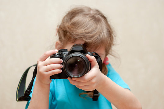  A child is aiming from the camera to take a picture. Little reporter takes a photo. SLR camera.