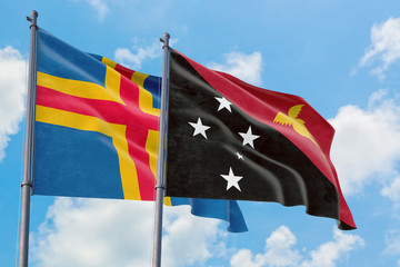 Papua New Guinea and Aland Islands flags waving in the wind against white cloudy blue sky together. Diplomacy concept, international relations.