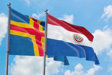 Paraguay and Aland Islands flags waving in the wind against white cloudy blue sky together....